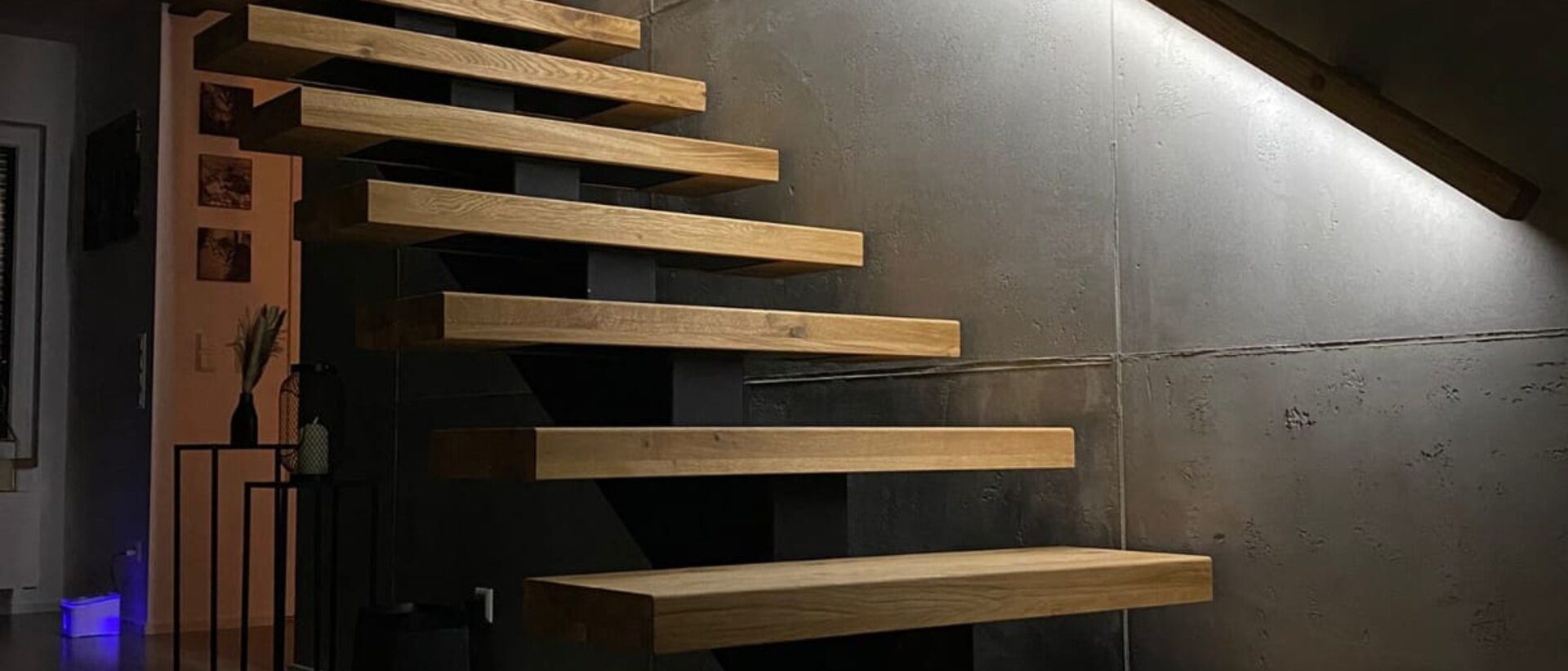 Einholmtreppe mit massiven Eichenstufen vor beleuchteter Sichtbetonwand in Epfenbach